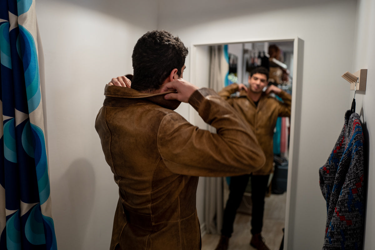 man trying on vintage leather jacket in the change room while looking in the mirror 